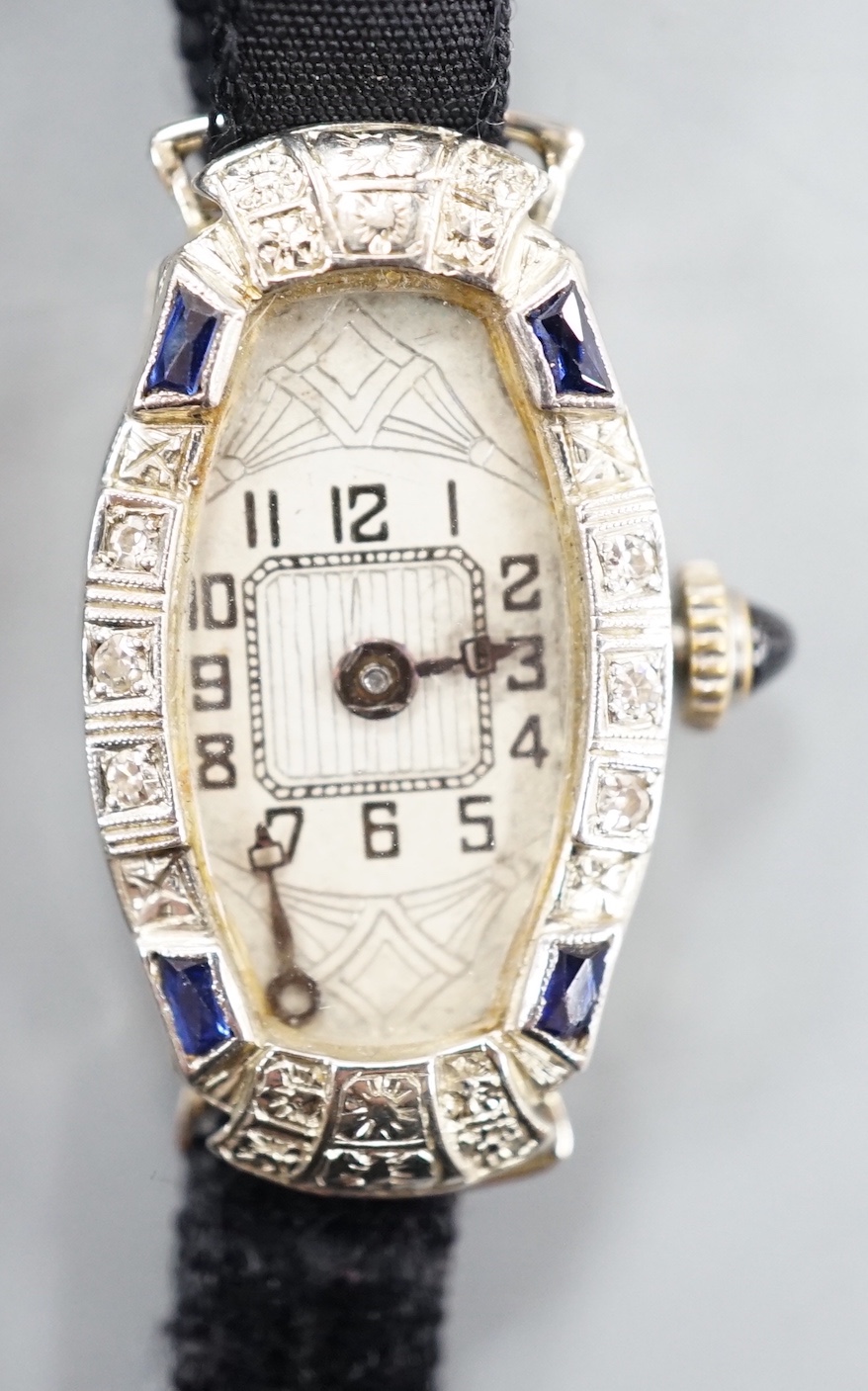 A lady's 18k white metal sapphire and diamond set manual wind cocktail watch, on fabric strap, gross weight 11.7 grams.